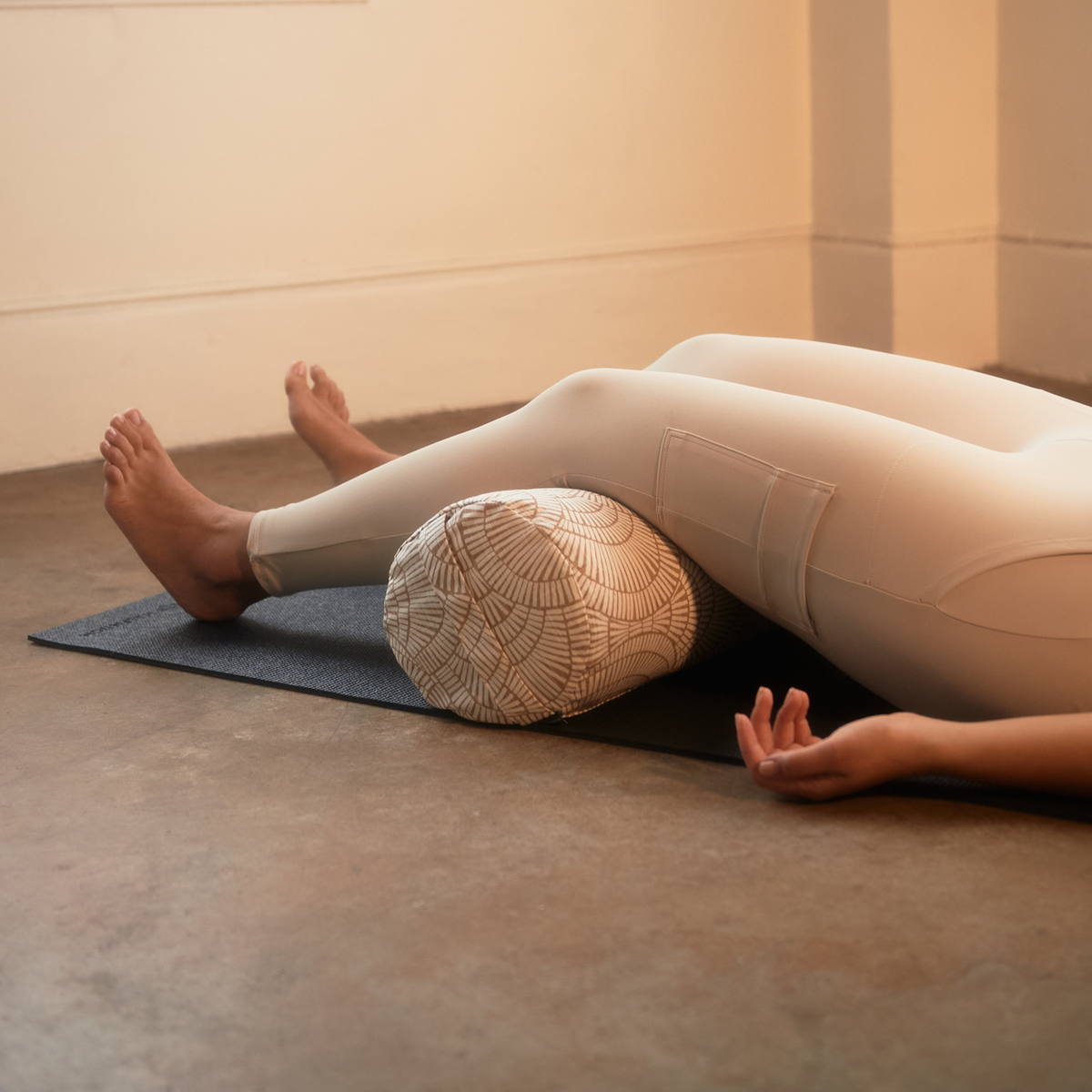 Person laying on floor with knees over bolster